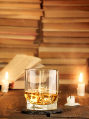 A glass of whiskey on the table with books and burning candles. Copy space, vertical photo.