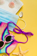Summer travel holiday vacation background flat lay. Pink sunglasses and towel, colorful swimsuit, starfish and seashells on yellow background.