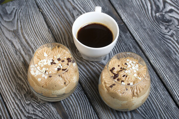 Peanut Trifle decorated with black and white chocolate. Nearby is a cup of coffee. Stands on pine boards.