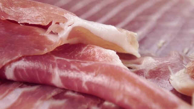 A fat piece of typical Spanish jamon is placed on a meat dish. The texture of a traditional gastronomic delicacy. Macro. Dolly shot