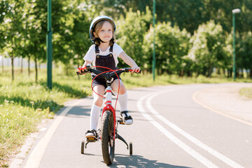 Fototapeta na wymiar Cheerful smiling girl in helmet on bicycle.