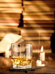 A glass of whiskey on the table with books and burning candles. Copy space, vertical photo.