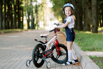 Fototapeta na wymiar Cheerful smiling girl in blue helmet standing near bicycle.