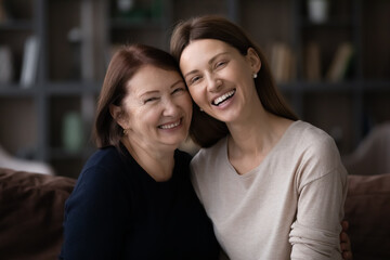 Portrait of happy two generations of women pose at home relax together. Smiling elderly Caucasian mother and adult grownup daughter rest on sofa, enjoy family weekend time. Unity concept.
