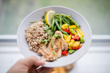 Hand holding a chicken and buckwheat dish with green beans