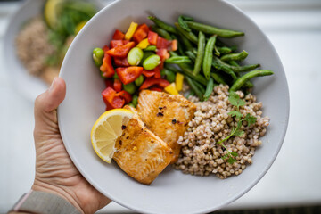 Hand holding salmon and buckwheat dish with green beans