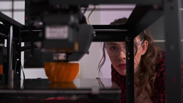 Female student in a modern classroom observing the printing process of a 3d model