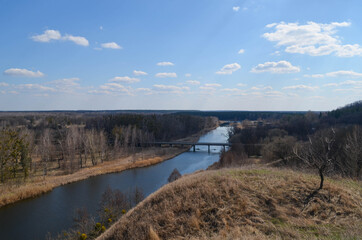 Top view on the great natural landscape in early spring. View on the river and bridge across it, on the forest and meadow. Drone view on nature scenery 