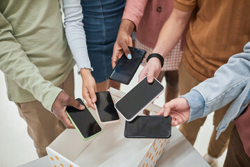Top view closeup of diverse group of teenagers putting smartphones in box in no gadget classroom at...