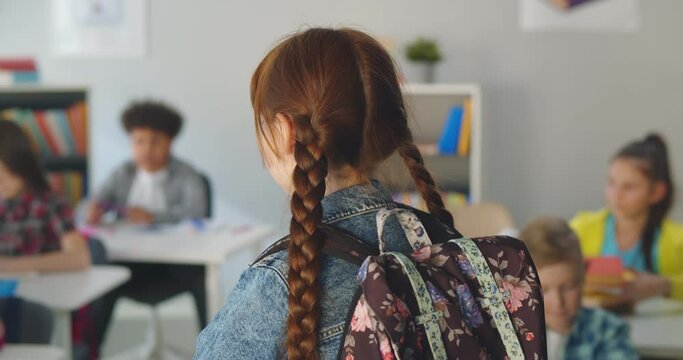 Back view of new girl standing in class looking at multiethnic classmates