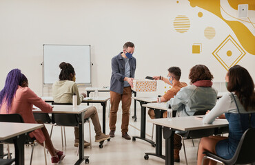 Wide angle view at male teacher collecting smartphones in school classroom with no-device policy,...