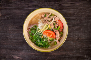 broth served with pieces of meat, tomatoes, rice noodles and chopped greens
