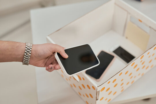 Close up of unrecognizable teenager putting smartphone in box in no gadget classroom at school, copy space