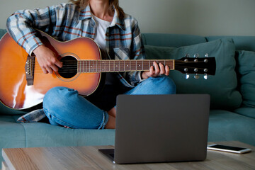 Obraz premium Music college hipster student in checkered shirt practicing acoustic guitar exercise, reading notes from laptop. Young woman taking an online musical courses, practicing at home. Background, close up