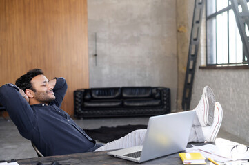 Satisfied and calm hindu mixed-race businessman takes a break on the workplace, leaned back in the...