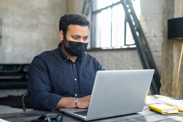 Hindu mixed-race male employee wearing protective face mask working in the office space. Measure for staying in safe of office staff from viral diseases during pandemic period