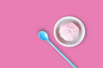 White cup of strawberry icecream and blue spoon serving on isolated pink background with blank copy space. Food, Dessert and advertisement Concept.