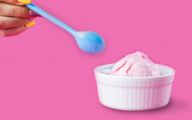 Close up to hand holding blue spoon with white cup of strawberry icecream on isolated pink background. Food, Dessert and Advertisement Concept.