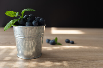 Fresh and sweet blueberry with mint in metal bucket on wooden table. Copy space.
