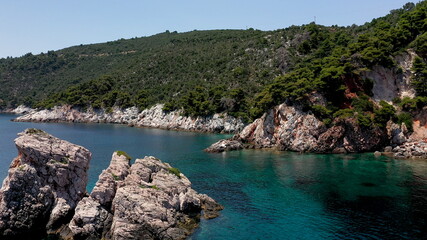 Fototapeta na wymiar Aerial drone views over a rocky coastline, crystal clear Aegean sea waters, touristic beaches and lots of greenery in Skopelos island, Greece. A typical view of many similar Greek islands.