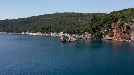 Naklejka premium Aerial drone views over a rocky coastline, crystal clear Aegean sea waters, touristic beaches and lots of greenery in Skopelos island, Greece. A typical view of many similar Greek islands.