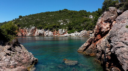 Obraz premium Aerial drone views over a rocky coastline, crystal clear Aegean sea waters, touristic beaches and lots of greenery in Skopelos island, Greece. A typical view of many similar Greek islands.