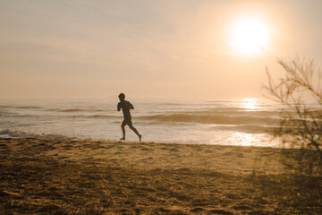 Fototapeta na wymiar silhouette man run on beach with sunrise and sea background