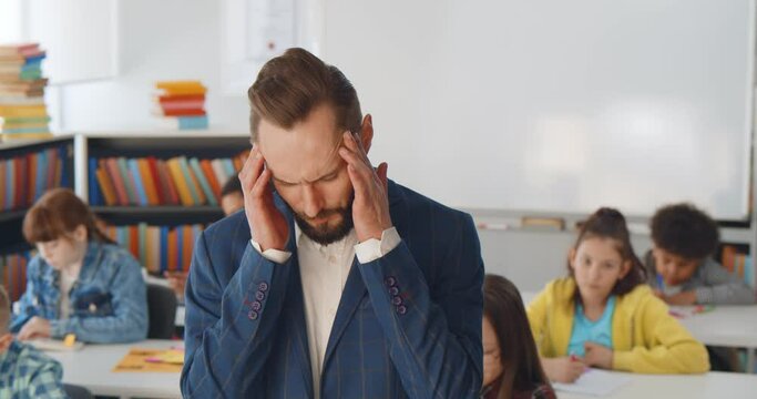 Tired teacher in suit suffering from headache standing in classroom