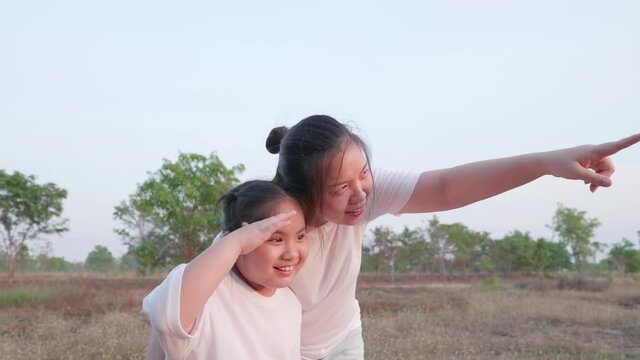 Front view of Asian mother point out and tell to daughter to looking far at field forest landscape then girl looking and point fingers follow mom. Mum and kid close embrace with smile and happy