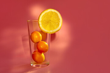golden oranges - kumquat with yellow lemon in glass on pink background. healthy lifestyle concept.