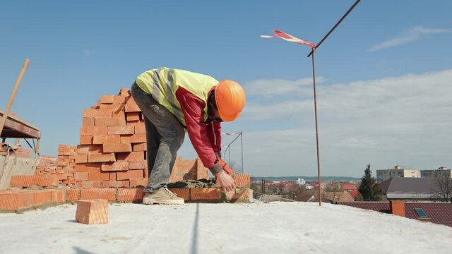 Close up of a man building a brick house. Laying red bricks on a construction site on a sunny day. House construction close up.