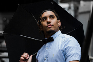 Model pose of a good looking mixed race man holding an umbrella in the rain wearing a shirt and bow...