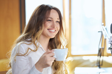 Side view of happy cute young woman in white shirt sitting in cafe and holding cup tasty coffee with good mood. Concept of drinking delicious hot drinks in free time. 