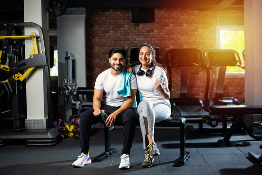 Portrait Of Indian Asian Young Couple Working Out Together In Gym, Training With Fitness Equipments