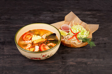 soup of sea foods with noodles, mussels, fish and tomatoes, served with lettuce and pepper