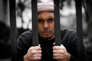 Angry Young male behind bars in Jail. hands holding metal bars