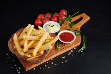 Homemade baked potato fries with mayonnaise, tomato sauce and rosemary on wooden board. tasty french fries on cutting board, in brown paper bag on black stone table background, unhealthy food.