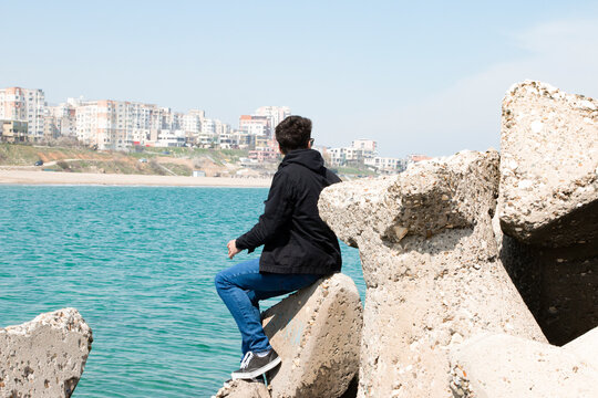 Young man sitting by rock looking out to sea