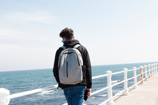 Young man walks  on footpath by sea against sky during sunny day 