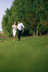 A loving couple wedding newlyweds in a white dress and a suit walk run smile happy on tall grass in the summer field on the mountain above the river. sunset.