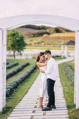 Young beautiful couple in love walking hugging in a summer green park near a white wooden arch. Wedding day, celebration.