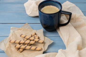 blue cup of coffee and waffle rolls on a wooden table