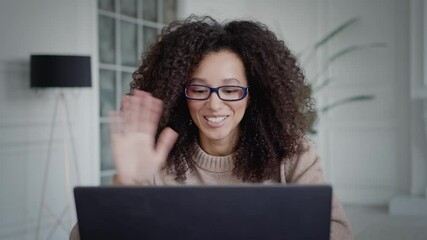 Young american black woman in eyeglasses sitting with laptop talking. Happy blogger speaking and gesturing, recording a video. Explain and teach things, video vlog in living home interior