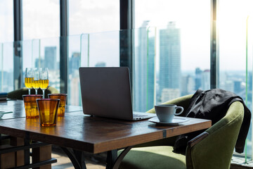 Scene of a dining table in a hotel lobby. The table is made of wood and has a lot of glass and bottle. The is a green fabric chair beside the table. The is also a black suit on the chair.