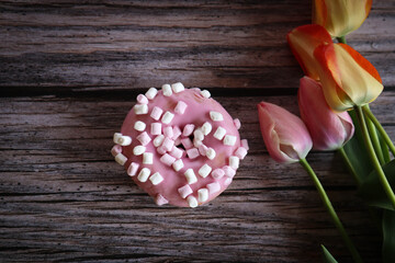 pink donut with marshmallows and  some tulips on the table.