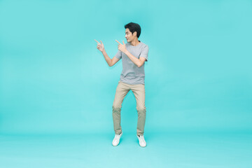 Fototapeta na wymiar Young Asian man jumping and pointing to empty copy space isolated on green background