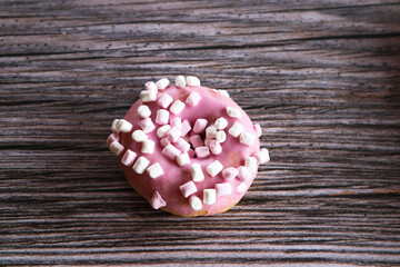 Pink donut with marshmallows on a wooden table.