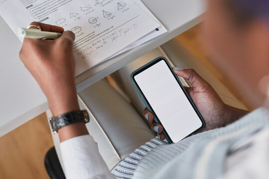 High angle closeup of unrecognizable African-American student holding smartphone with blank screen while taking math test in school, cheating at exam concept, copy space