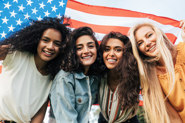 Four diverse women friends looking at the camera under the American flag. Cheerful females...