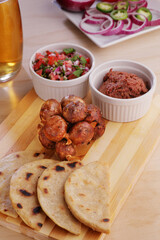 A traditional latin american chorizo links served in a wooden board next to some tortillas and condiments.